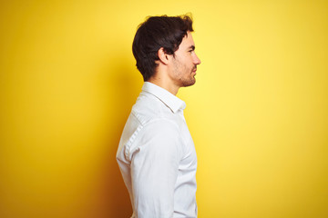 Young handsome businessman wearing elegant shirt standing over isolated yellow background looking...