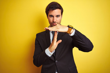 Young handsome businessman wearing suit and tie standing over isolated yellow background Doing time...