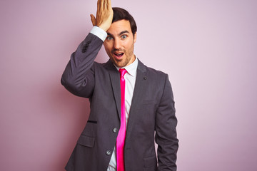 Young handsome businessman wearing suit and tie standing over isolated pink background surprised with hand on head for mistake, remember error. Forgot, bad memory concept.