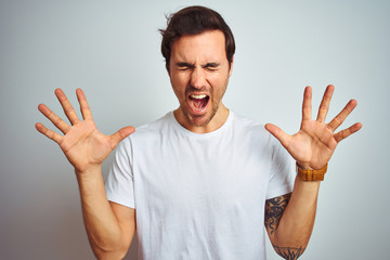 Naklejka premium Young handsome man with tattoo wearing casual t-shirt over isolated white background celebrating mad and crazy for success with arms raised and closed eyes screaming excited. Winner concept