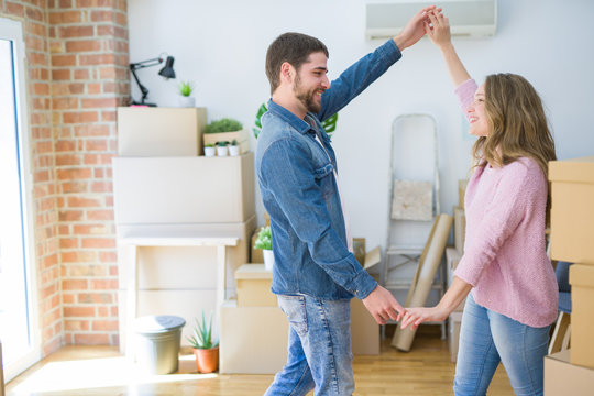 Young couple dancing celebrating moving to new apartment around cardboard boxes