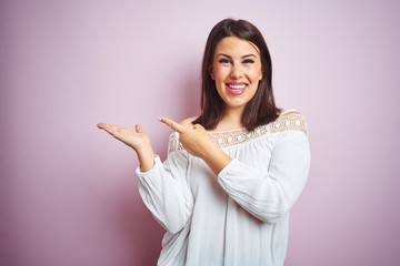 Young beautiful brunette woman over pink isolated background amazed and smiling to the camera while presenting with hand and pointing with finger.