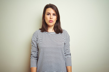 Obraz premium Young beautiful brunette woman wearing striped sweater over white isolated background with serious expression on face. Simple and natural looking at the camera.