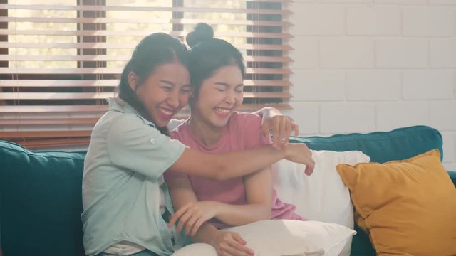 Young Lesbian lgbtq Asian women couple hug and kiss at home. Attractive Asian lover pride female happy relax spend romantic time together while lying sofa in living room concept. Slow motion.