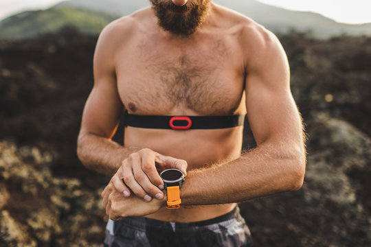 Athletic man watching training results on smart watch or fitness tracker. Running topless and using chest heart rate monitor. Body close-up.