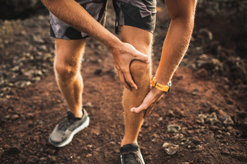Knee injury on running outdoors. Man holding knee by hands close-up and suffering with pain. Sprain ligament or meniscus problem. - obrazy, fototapety, plakaty