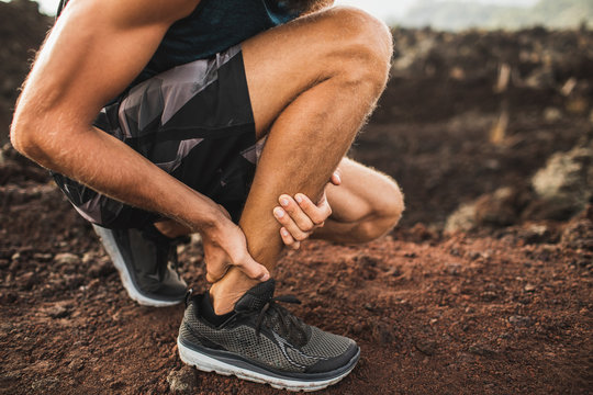 Achilles injury on running outdoors. Man holding Achilles tendon by hands close-up and suffering with pain. Sprain ligament or Achilles tendonitis.