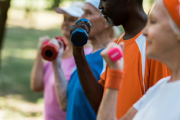 cropped view of multicultural group of senior men and women exercising with dumbbells