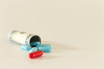 100 dollar bill curled up with legal drugs called pills or colored medications on a white neutral background. Concept of drug addiction and health cost.