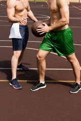 Fototapeta premium partial view of two shirtless sportsmen playing basketball at basketball court in sunny day