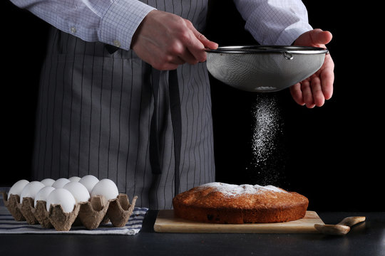 chef pouring powdered sugar on tasty pie on dark background. ched processing pie or cake