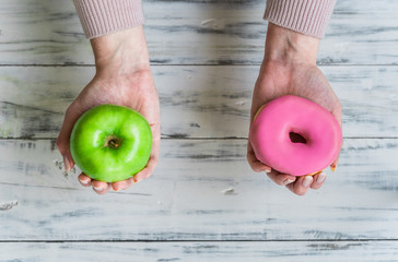 Young woman holding a doughnut and green apple in her hands. Concept of healthy and unhealthy food,...
