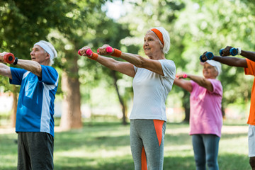 selective focus of senior pensioners exercising with dumbbells in park