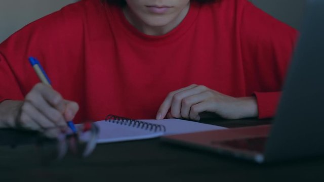 Concept of home education. Close up - woman hands overwrites in notepad information from the laptop.