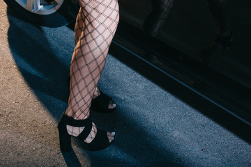 cropped view of woman in mesh stockings standing in shoes near car