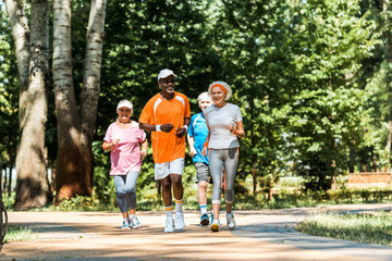 Obraz premium cheerful multicultural and senior men and women in sportswear running in park