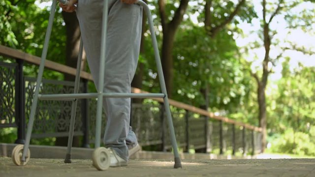 Legs of patient slowly moving with help of walking frame in hospital park