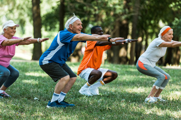selective focus of multicultural senior mean and women doing sit ups on grass