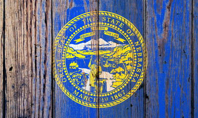 Nebraska US state national flag on a gray wooden boards background on the day of independence in different colors of blue red and yellow. Political and religious disputes, customs and delivery.