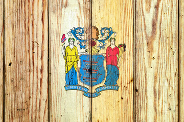 New Jersey US state national flag on a gray wooden boards background on the day of independence in different colors of blue red and yellow. Political and religious disputes, customs and delivery.