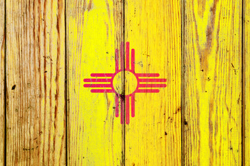 New Mexico US state national flag on a gray wooden boards background on the day of independence in different colors of blue red and yellow. Political and religious disputes, customs and delivery.