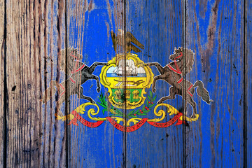 Pennsylvania US state national flag on a gray wooden boards background on the day of independence in different colors of blue red and yellow. Political and religious disputes, customs and delivery.