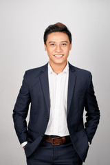 A young Asian man in suit put both hands in his pants pocket, isolated on a white background.