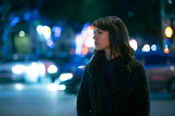 Caucasian pedestrian woman walking the street at night in the city with moving cars in the...