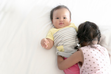 Two sisters cuddle and roll over on white bed after wake up in the morning. Sisters showing love to each other.