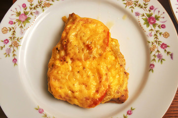 A piece of fried meat with tomatoes and cheese on a plate with oil drops, top view