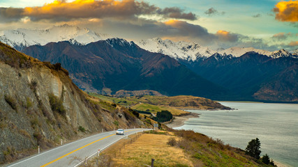 One car ran on a road on the edge of the lake. The background is a great mountain in the evening. Beautiful Clouds at Lake Hawea Lookout in Wanaka Otago, Newzealand