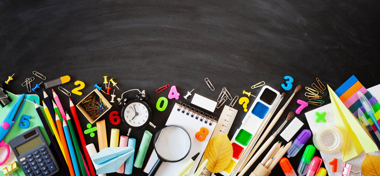 Set of stationery, alarm clock and supplies on blackboard background. Back to school concept. Banner format. Top view.