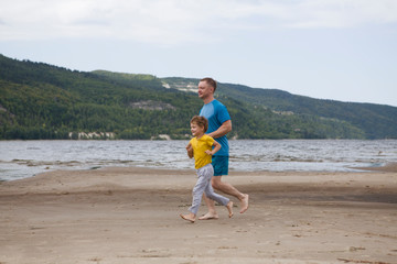  Father and son spend time together and lead a healthy lifestyle outdoors. Man and boy run on the beach in the summer.