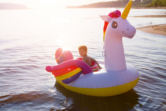 Kid boy with Unicorn swim tube on the beach. Inflatable unicorn. holiday and travel concept.