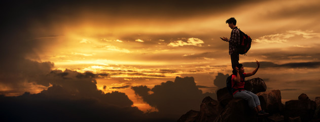 Silhouette of Hikers climbing up mountain cliff in sunset with live chat smartphone. Concept of...