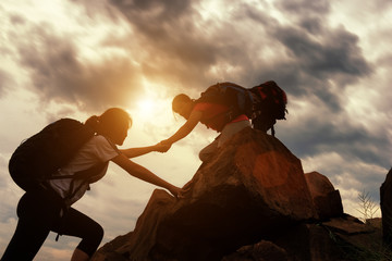 Hiking team helping each other while climbing up in a sunset. The concept of aid. - obrazy, fototapety, plakaty