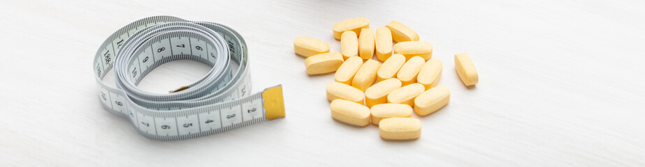 Yellow diet pills lie on a white table next to a measuring tape. Concept of weight loss with the help of medicines.