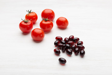 Tomatoes lie on a white table next to vitamins in the form of jelly on a white table. Concept of vitamins and minerals.