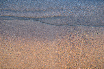 Fototapeta na wymiar Sea wave and sand seashore. Golden sun light over the sea ocean waves. MIrror reflection on water surface. Macro close up.