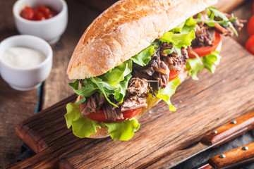 Beef sandwich with tomato and salad on wooden cutting board with ingredients.