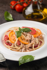 spaghetti with tuna, tomatoes and garlic sauce on white plate over dark background