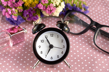 Alarm clock, black glasses and perfume bottle on napkin background composition.