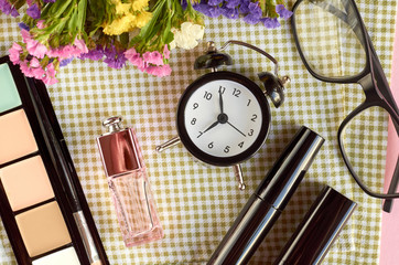 Alarm clock with flowers, mascara and perfume bottle on napkon background composition.