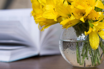 blue coffee mug, yellow flowers in transparent bowl and a book on a wooden table