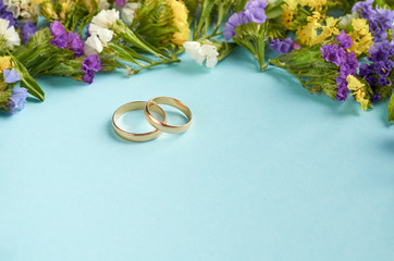 Golden rings with colored flowers on blue background composition, wedding template.