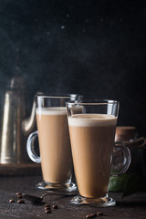 Two glasses with cold coffee latte macchiato on table against black background