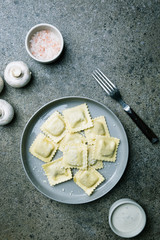 Plate of ravioli with mushrooms and cheese decorated by basil on dark stone background, top view
