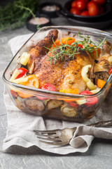 Baked whole chicken with vegetables and herbs close-up on a plate on a table.