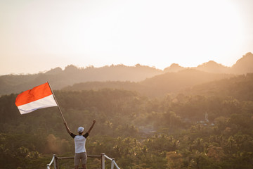 Fototapeta na wymiar portrait of man on top of the hill in the morning rising indonesian flag celebrating independence day