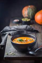 Pumpkin soup in a black plate on dark wooden background. Autumn decorations.